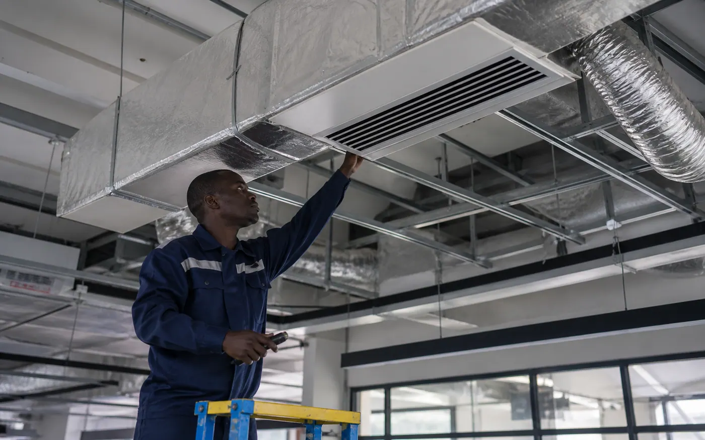 Kenyan HVAC technician checking insulated ducted air conditioning and linear diffusers